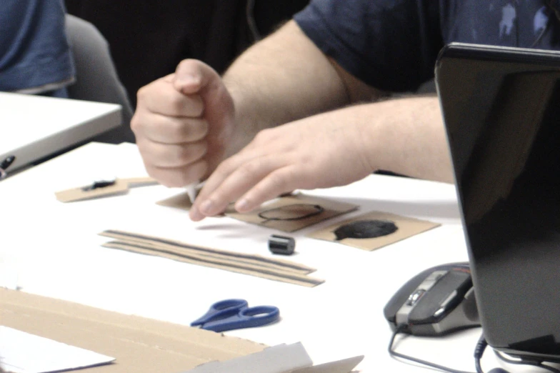 a man at a table with scissors in front of a laptop