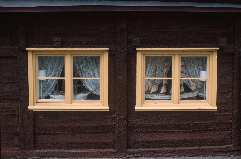 a wooden building with two windows and some curtains