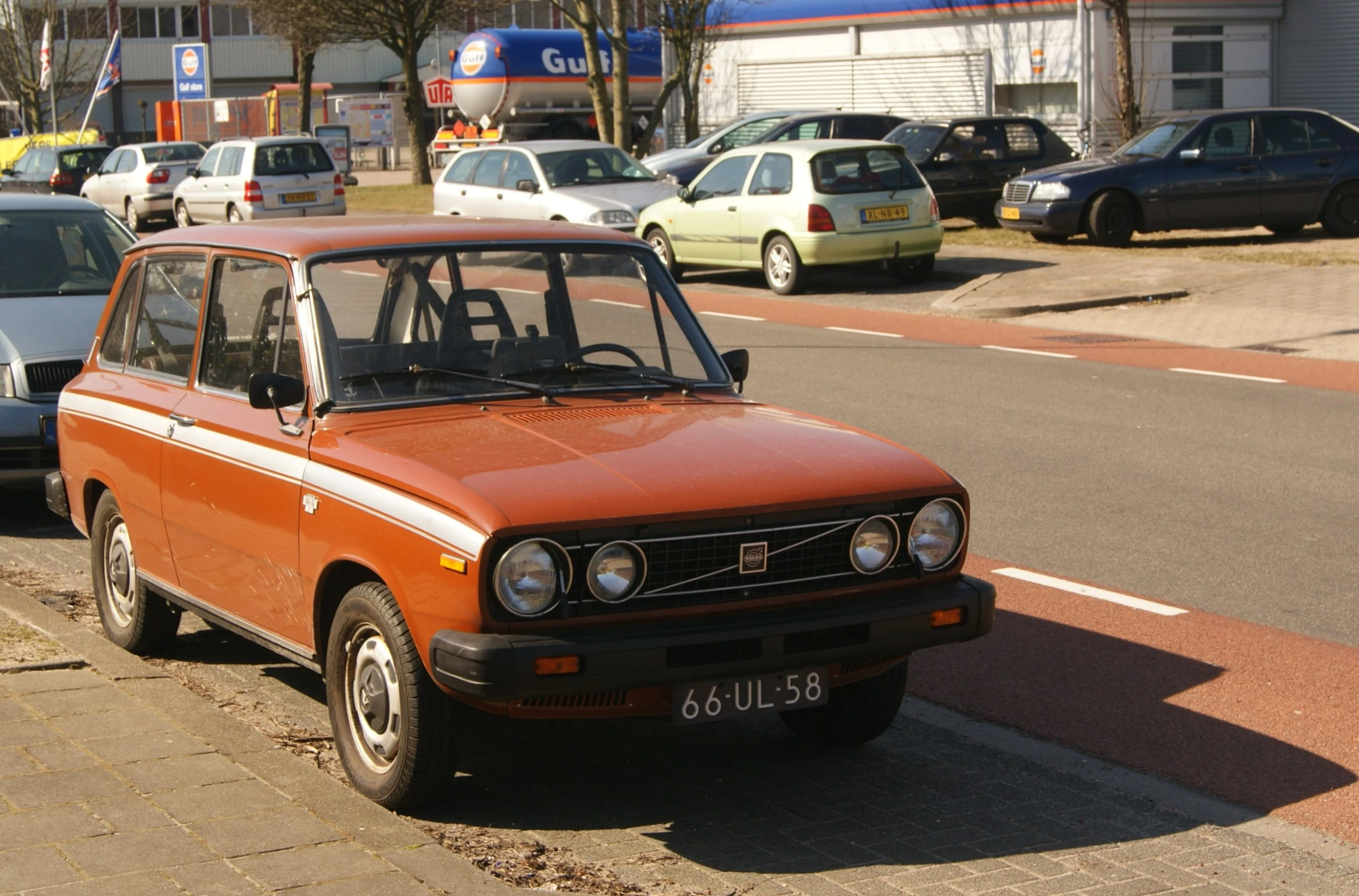 an orange and brown station wagon on sidewalk with cars in background