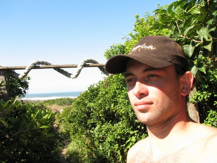 a man in a cap on the edge of a fence near trees