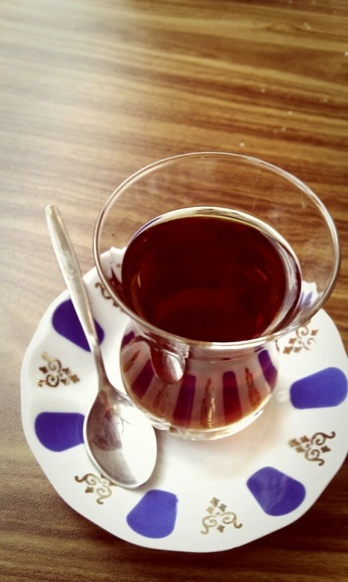 a glass tea cup filled with liquid next to a spoon on a plate