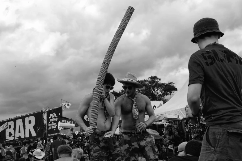 people stand in a group with one man without a shirt holding a large, ironing sword