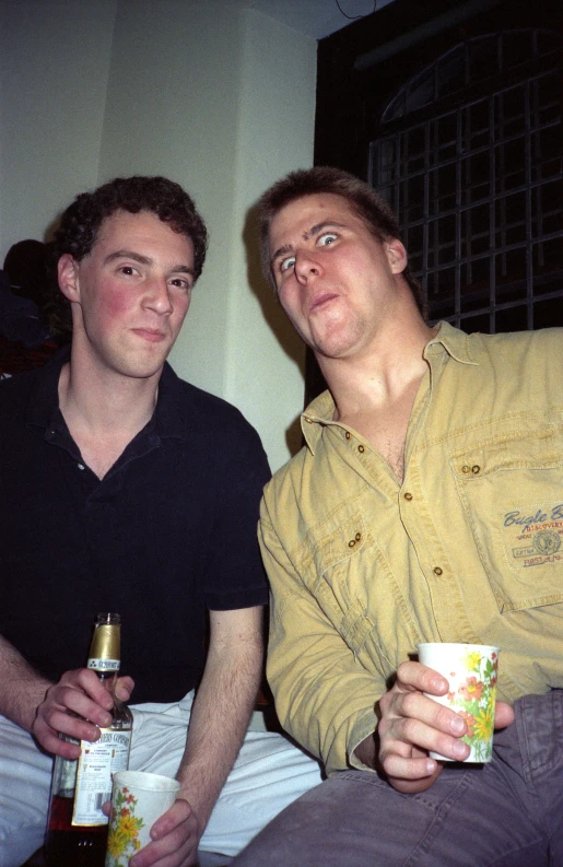 two young men sit next to each other drinking beer