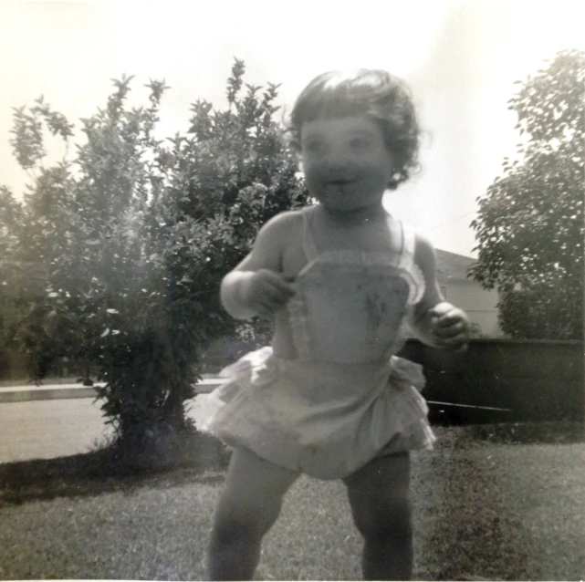 a girl standing in front of a bush holding a frisbee