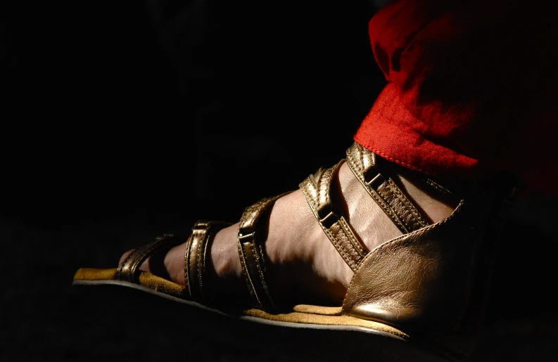 the foot of a person with metallic shoes and red sweater