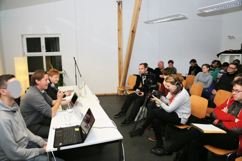 several people sitting in chairs with one woman holding a camera, looking at another person's laptop