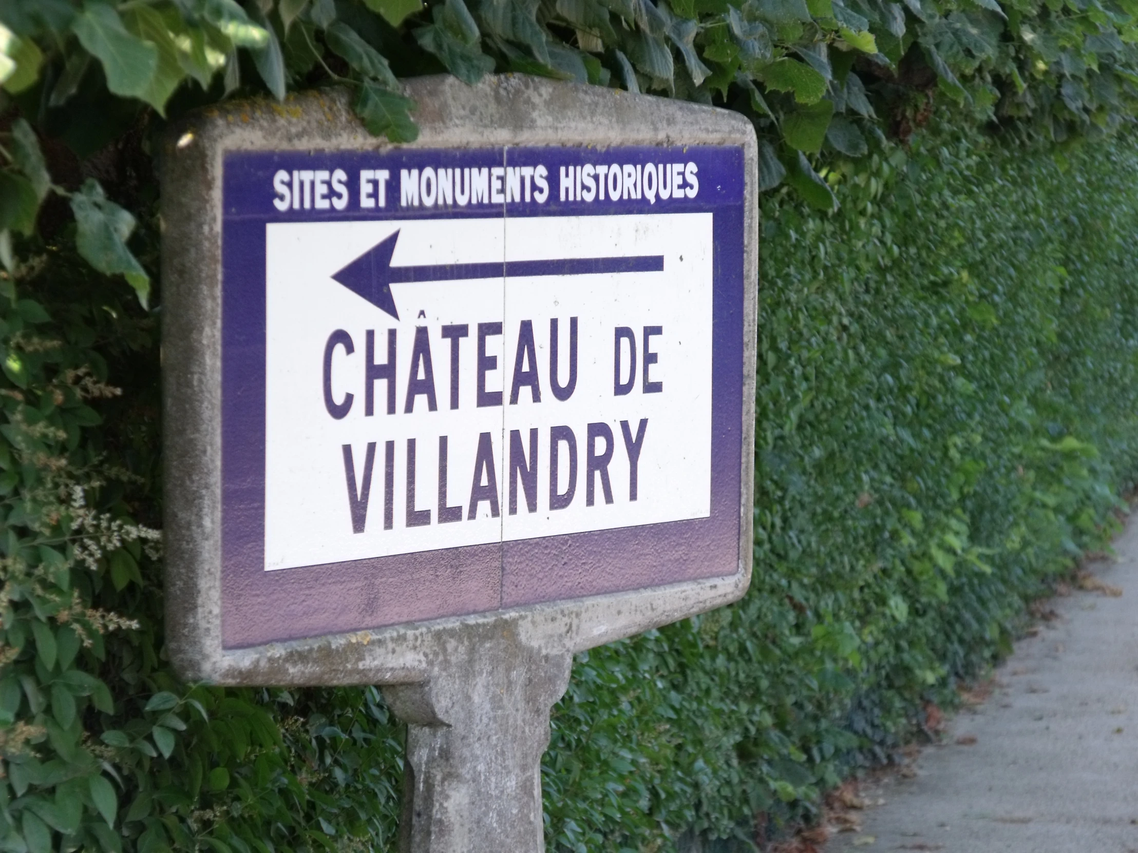 a sign pointing to a street in front of a hedges