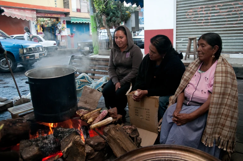 women roasting some kind of meat in a wooden fire pit