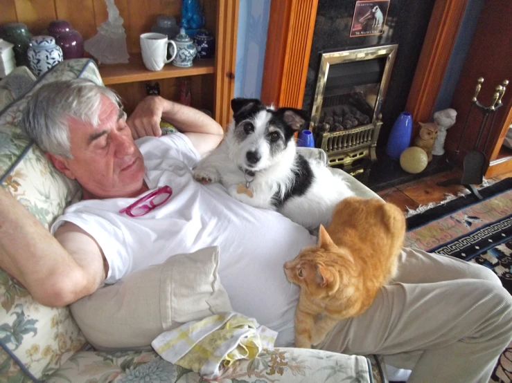 an old man lying down in bed with two dogs and a cat