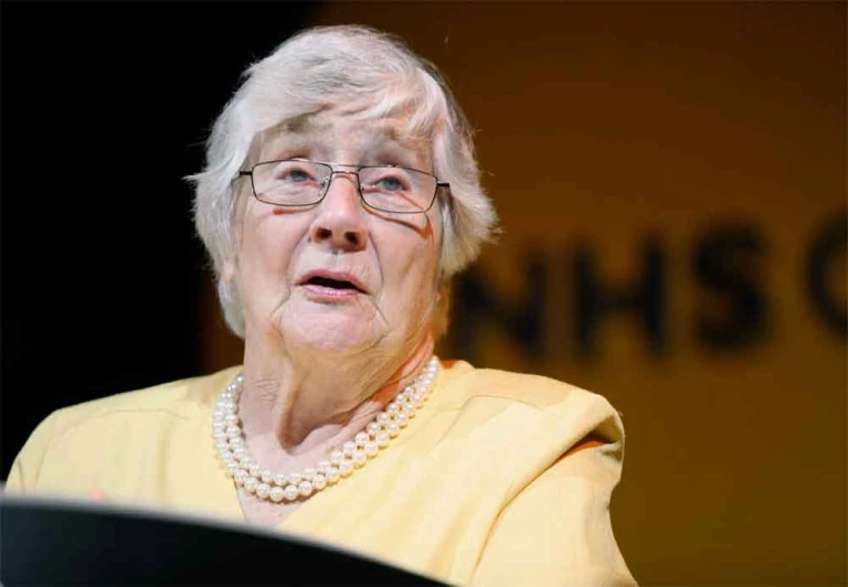 an older woman in glasses looks up at the microphone