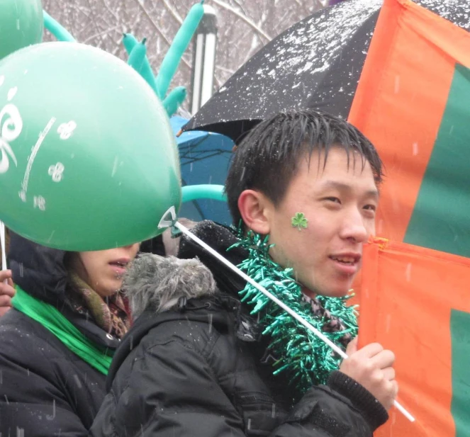 a man is standing under an umbrella holding some green balloons