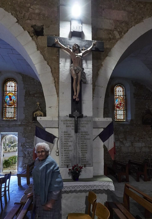 an older woman stands in front of a statue of jesus on the cross