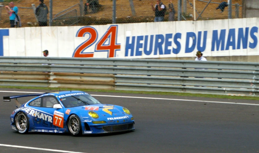 blue sports car speeds around a corner while people watch