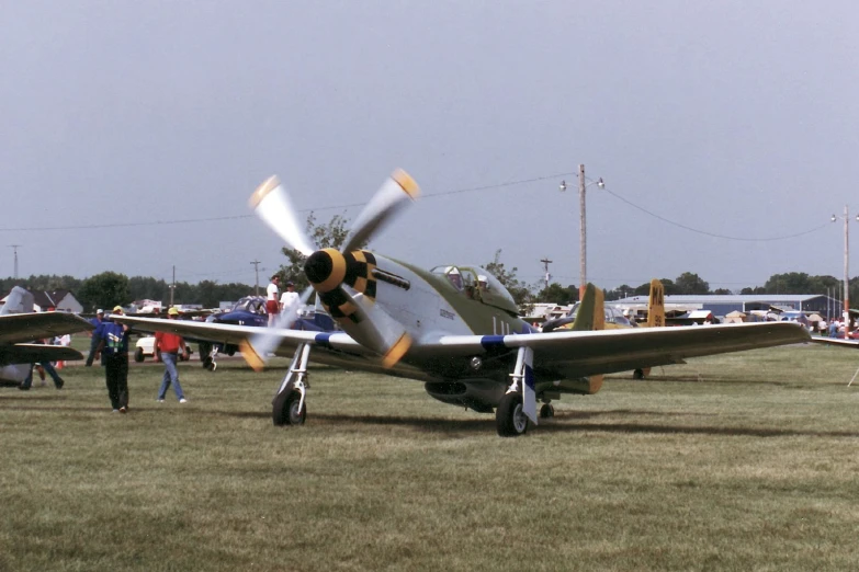 people gather around an old fashioned airplane in the grass