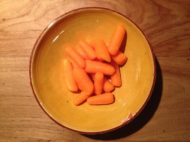 a yellow bowl filled with a group of orange baby carrots
