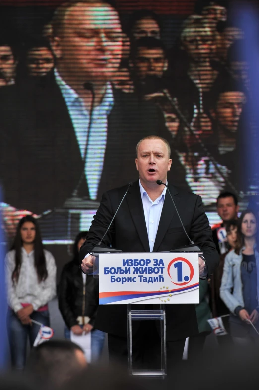 a man holding a microphone up as he speaks to an audience