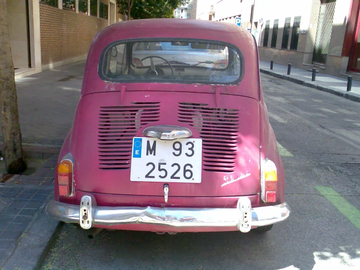 an old pink car sits on the sidewalk