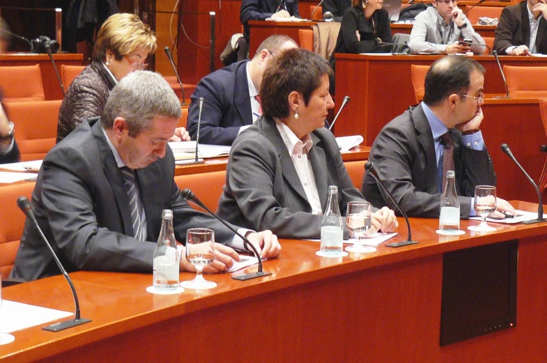 three men sitting at a wooden table, wearing business suits