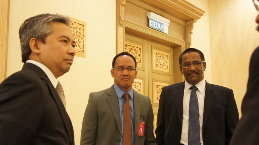 three men standing around talking in a hallway