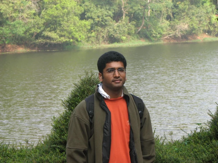 a man standing beside a lake wearing an orange and black shirt