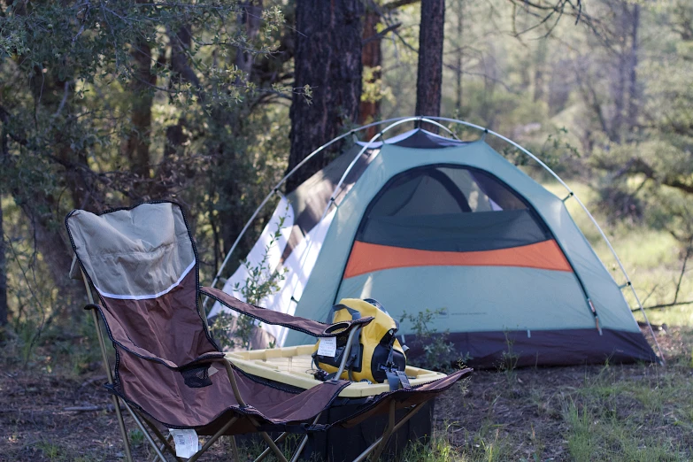 a tent, bench and chair in the woods