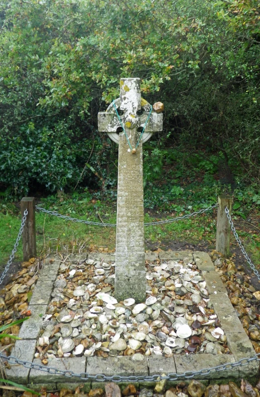 a cross with an intricate stone base surrounded by leaves and flowers