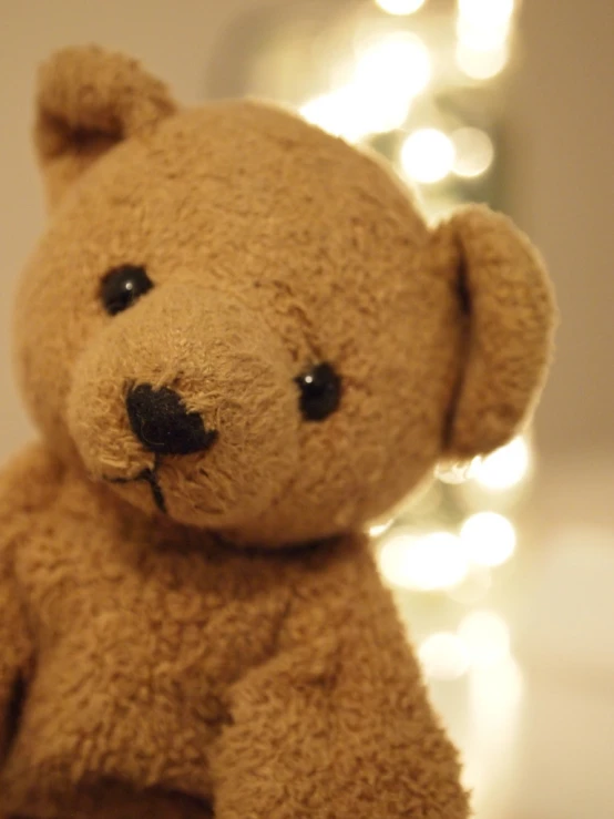 an adorable little teddy bear sitting near a lighted wall