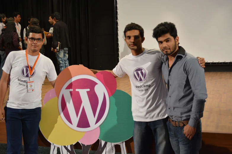 three men posing in front of a wooden sign with the wordpress logo on it
