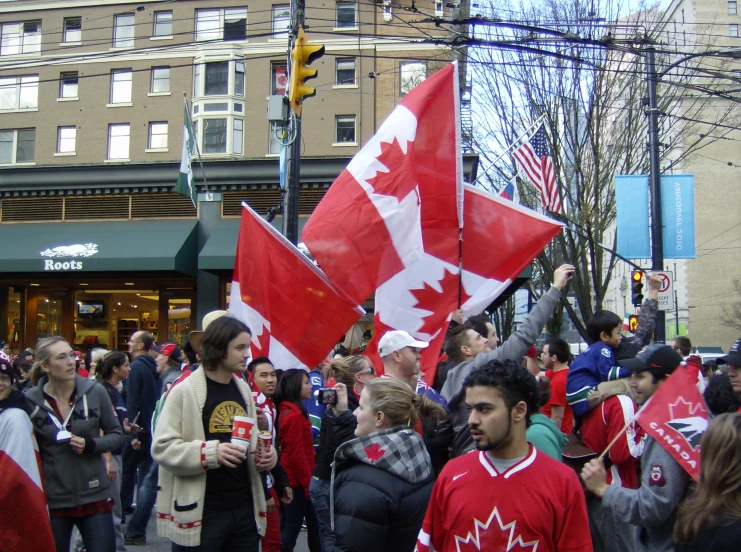 a crowd of people walk down the street holding canadian and american flags