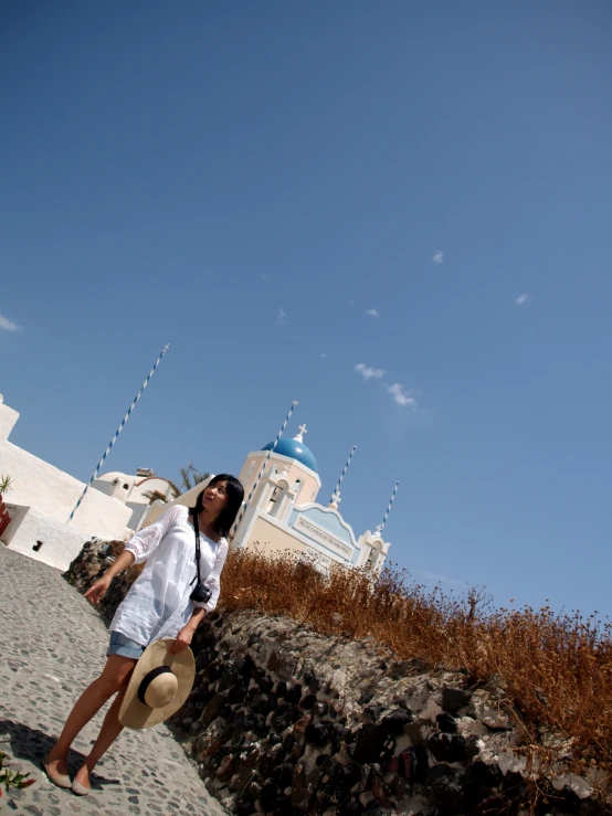 a girl in white holding a hat while standing on the beach