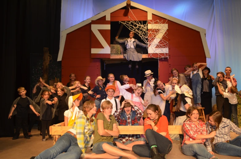 many children are on the stage with an assembly and audience