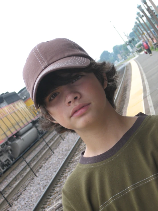 a boy poses for a po near some train tracks