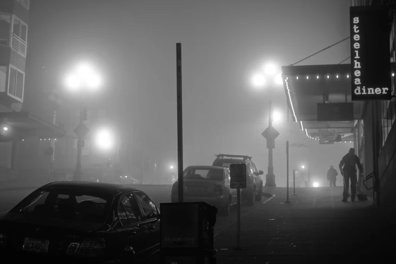 a foggy city street with streetlights and cars parked on the side