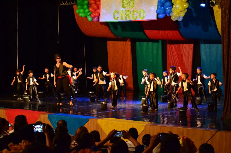 a group of children wearing costumes standing on stage with their arms in the air