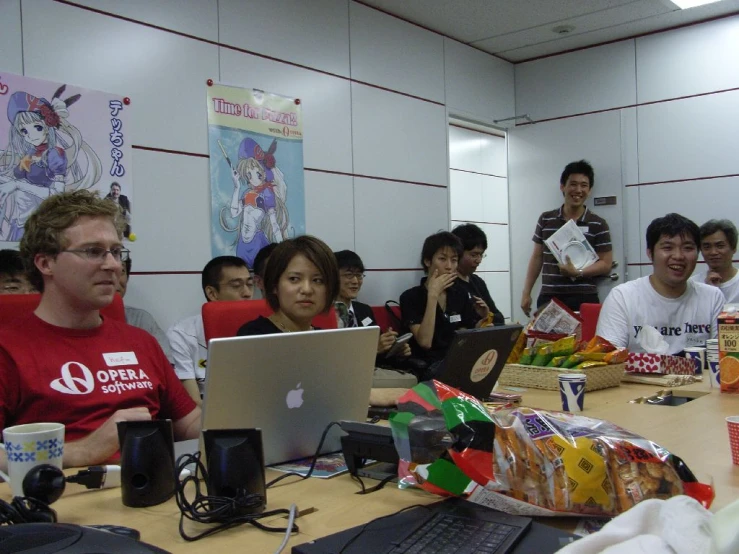 several people gathered at a long table while looking at an apple computer