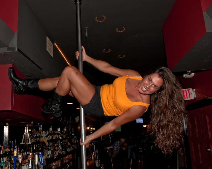 a woman in an orange shirt and short shorts hangs from a pole on a bar