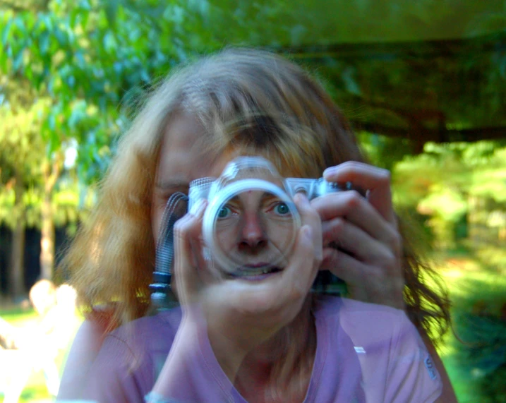 the girl holds a camera and is reflected in a circular glass