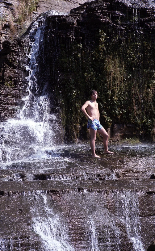 a man standing in the water by a waterfall