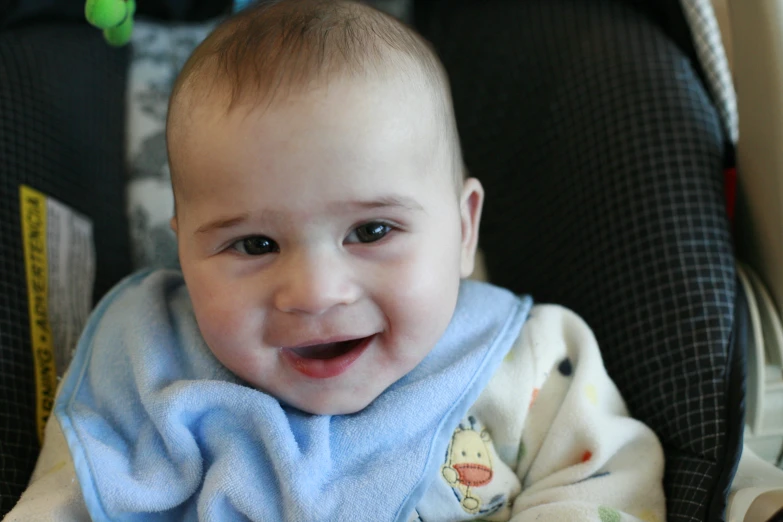a baby with a blanket around his neck smiles while sitting in a chair