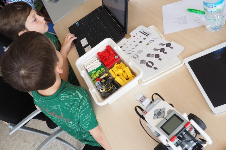 two children sit in front of their computers looking at their toy