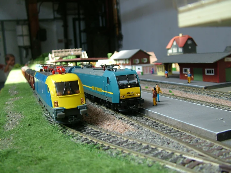 toy trains sit on tracks while people walk by