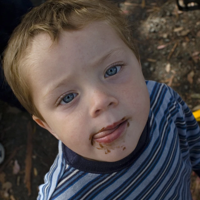 the boy is outside and his tongue has messy dirt on it