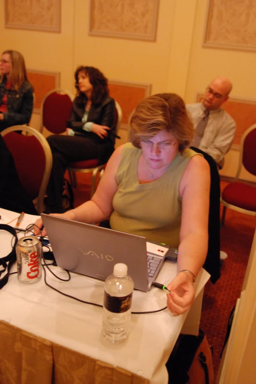 woman at laptop looking at camera with other people in background