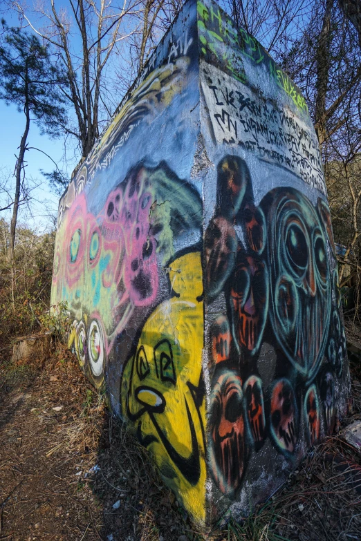 a stone wall has grafitti, and it has trees in the back