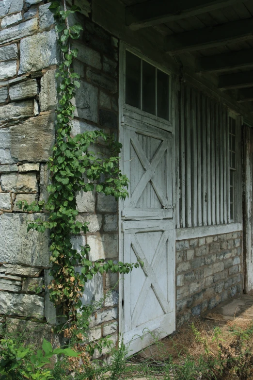 the wooden door is next to an old building with a brick wall and ivy growing up the outside of the barn