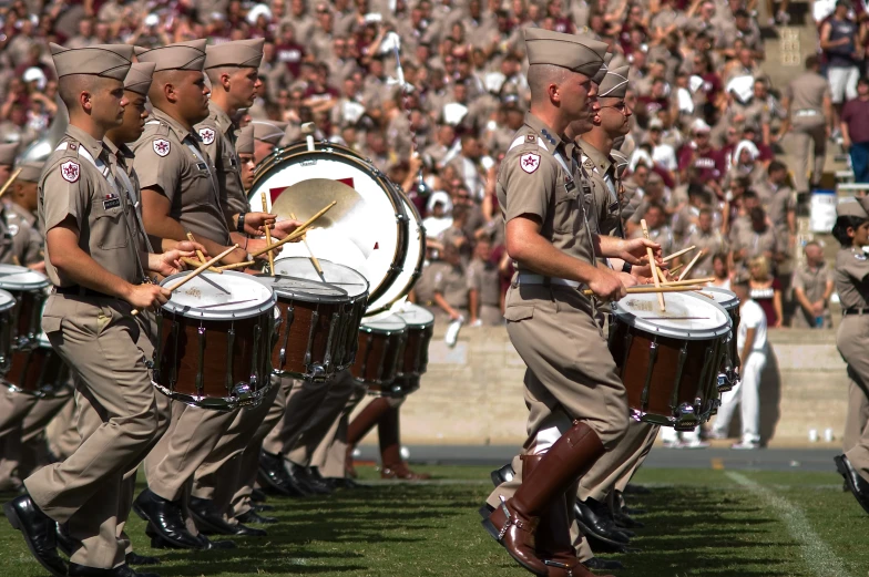 military marching band marching on football field with people in the background