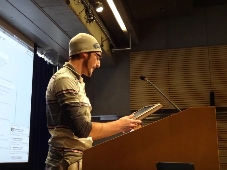 a man is standing at a podium and looking down at a sheet of paper in his hand