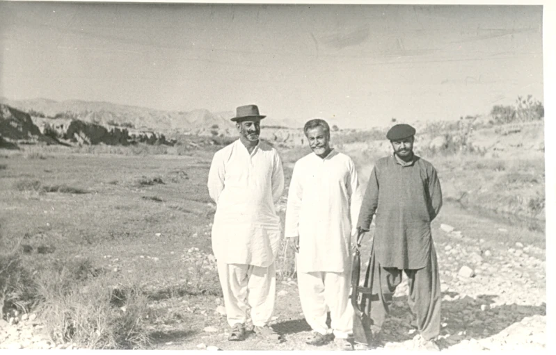 three men stand in an open field posing for the camera