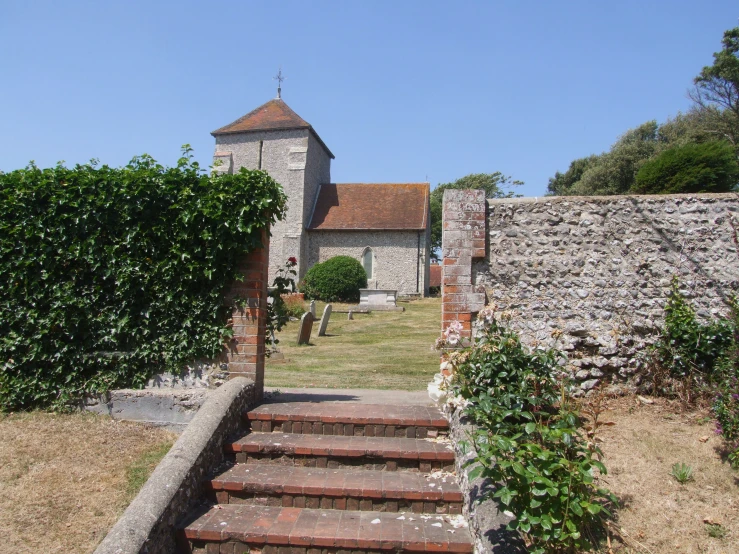 a church with a steeple and gate beside some bushes