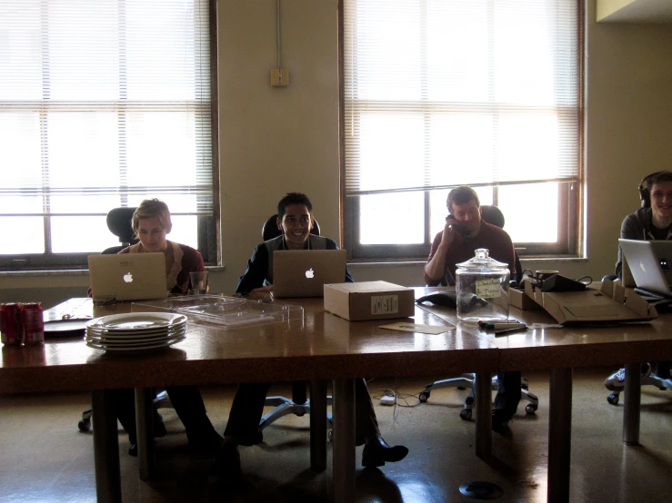 a group of people sitting around a table with laptop computers on it